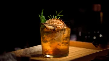 Ein Cocktailglas mit Eis, garniert mit Kräutern, steht auf einem Holztablett.